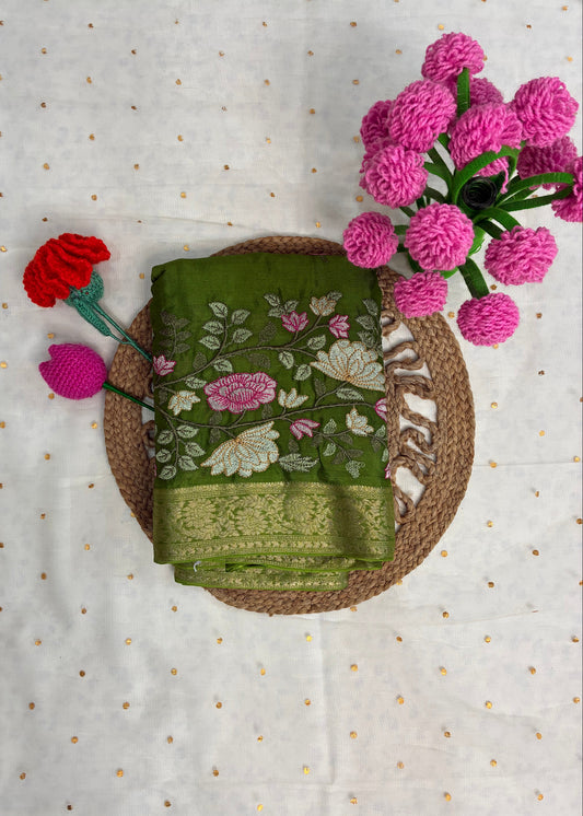 Green embroidered fabric with pink flowers on a textured white background