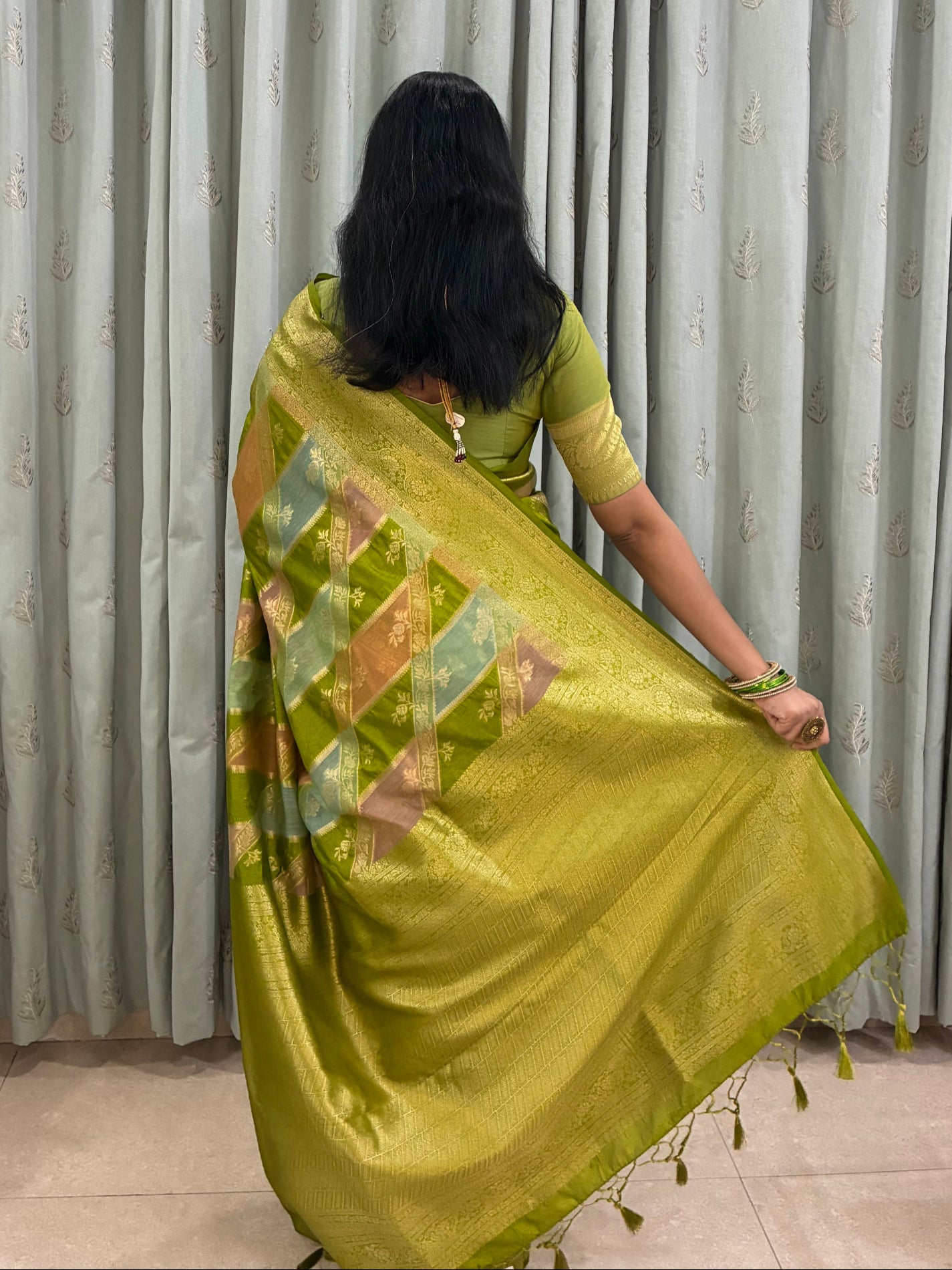 Person in a green saree with a floral pattern standing in front of a metal shutter.