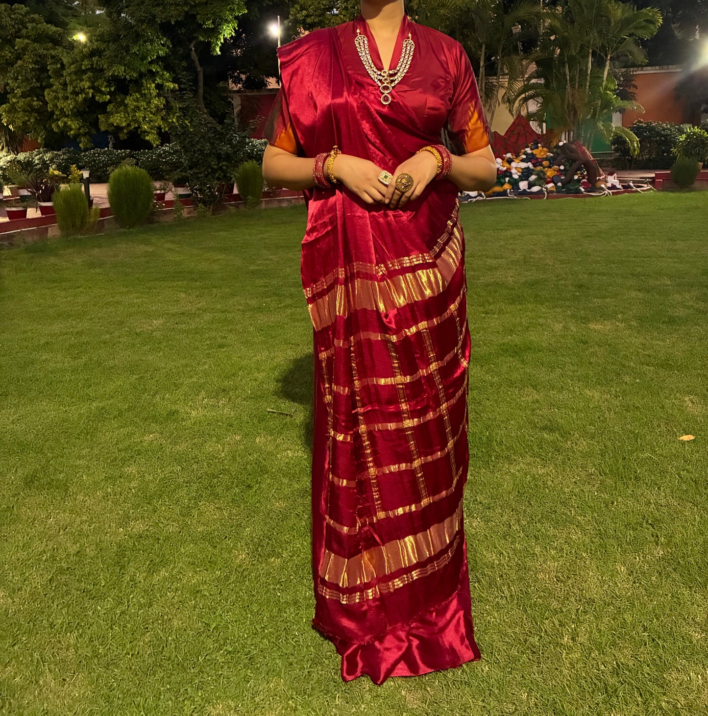 Woman in a red saree standing on grass with trees in the background