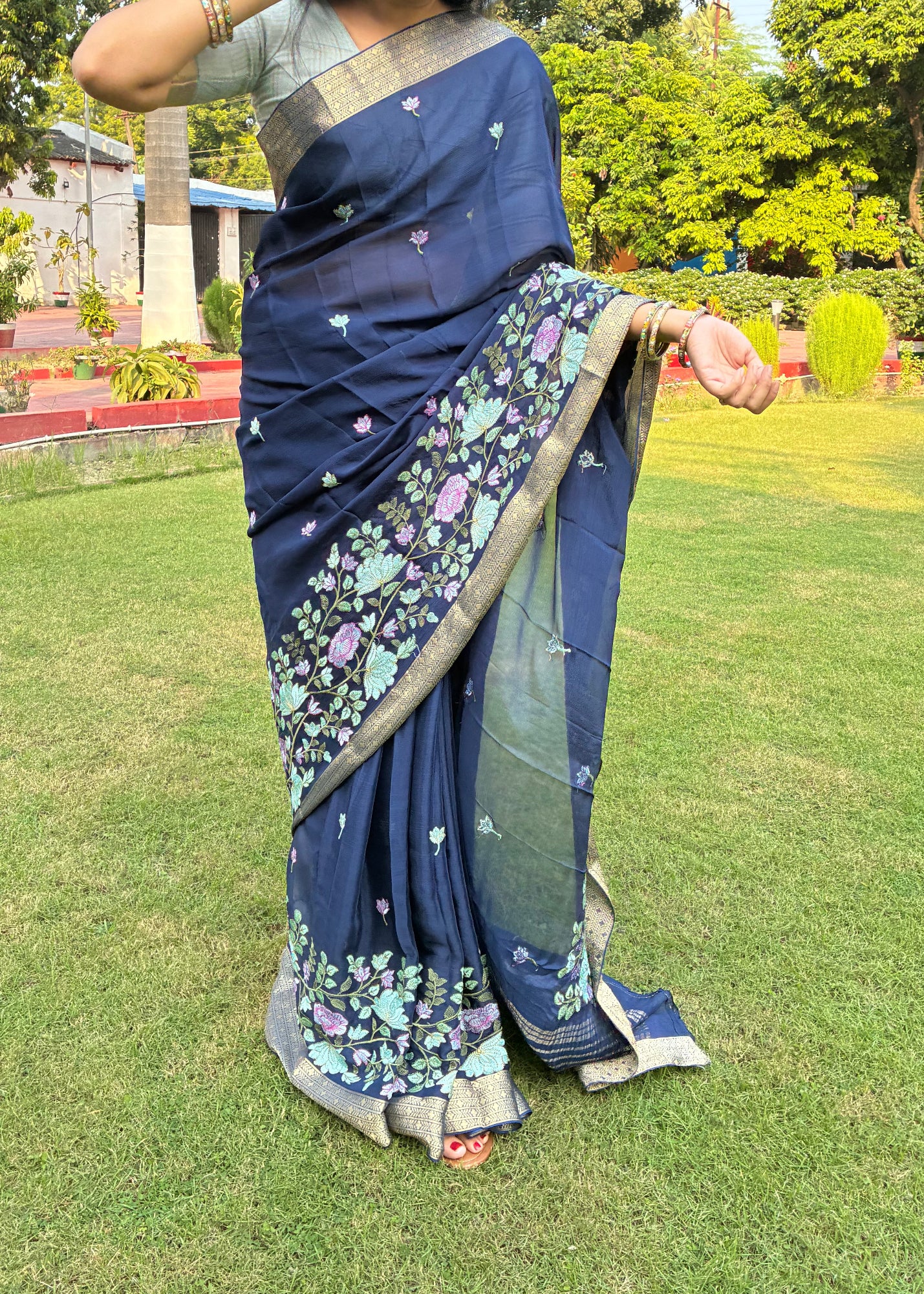 Woman in a blue saree with a floral pattern standing on grass with trees in the background