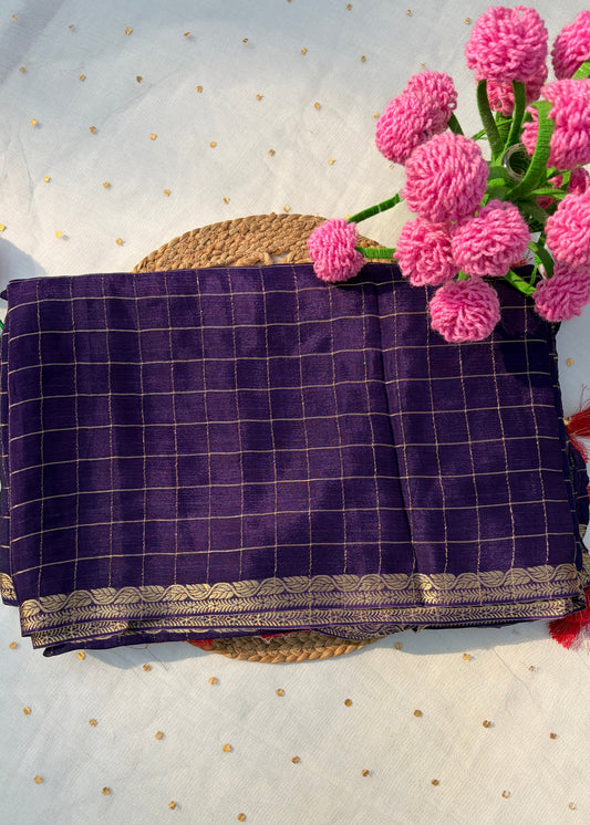 Purple checkered fabric with gold accents on a textured white surface with pink flowers.