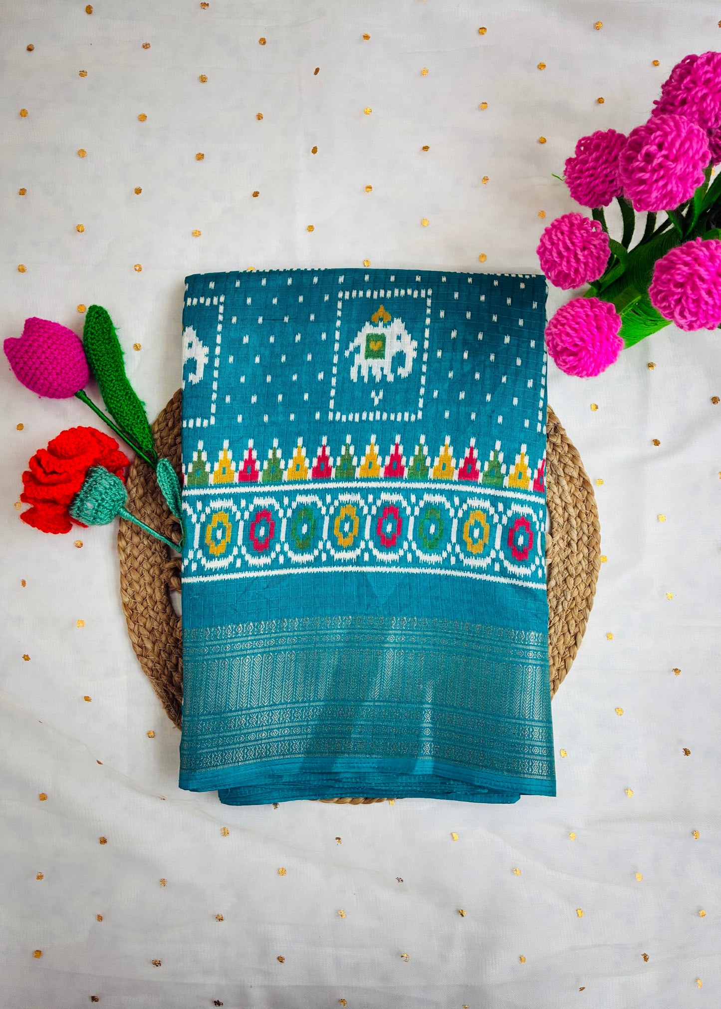 Teal fabric with colorful patterns on a white background with pink flowers.