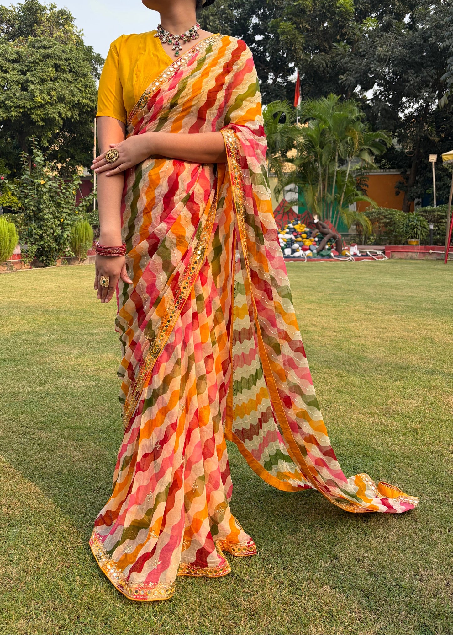 Woman in a colorful saree standing on grass with trees in the background