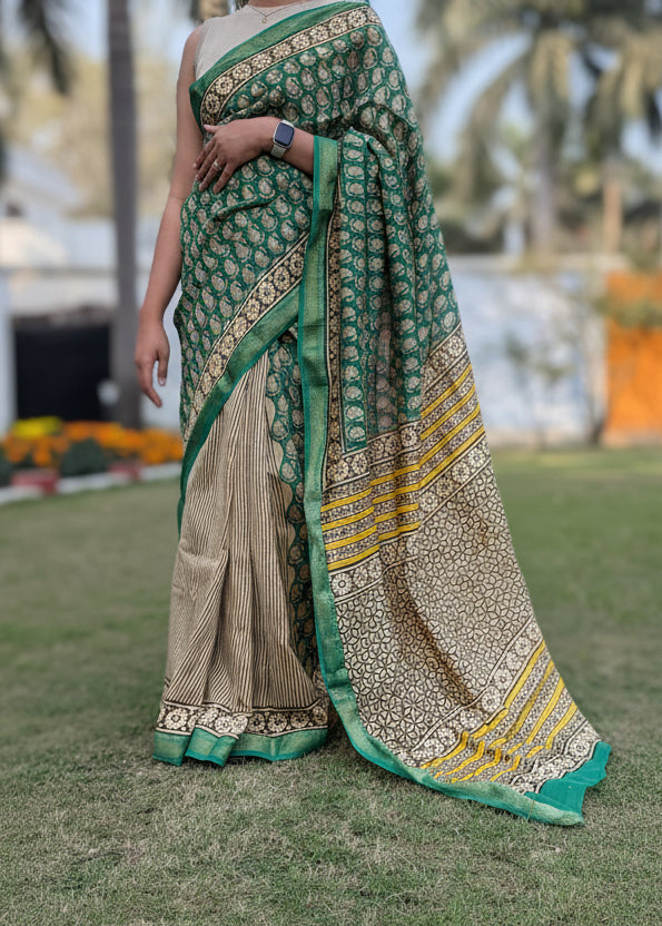 Person wearing a green and beige saree with a patterned border in an outdoor setting.