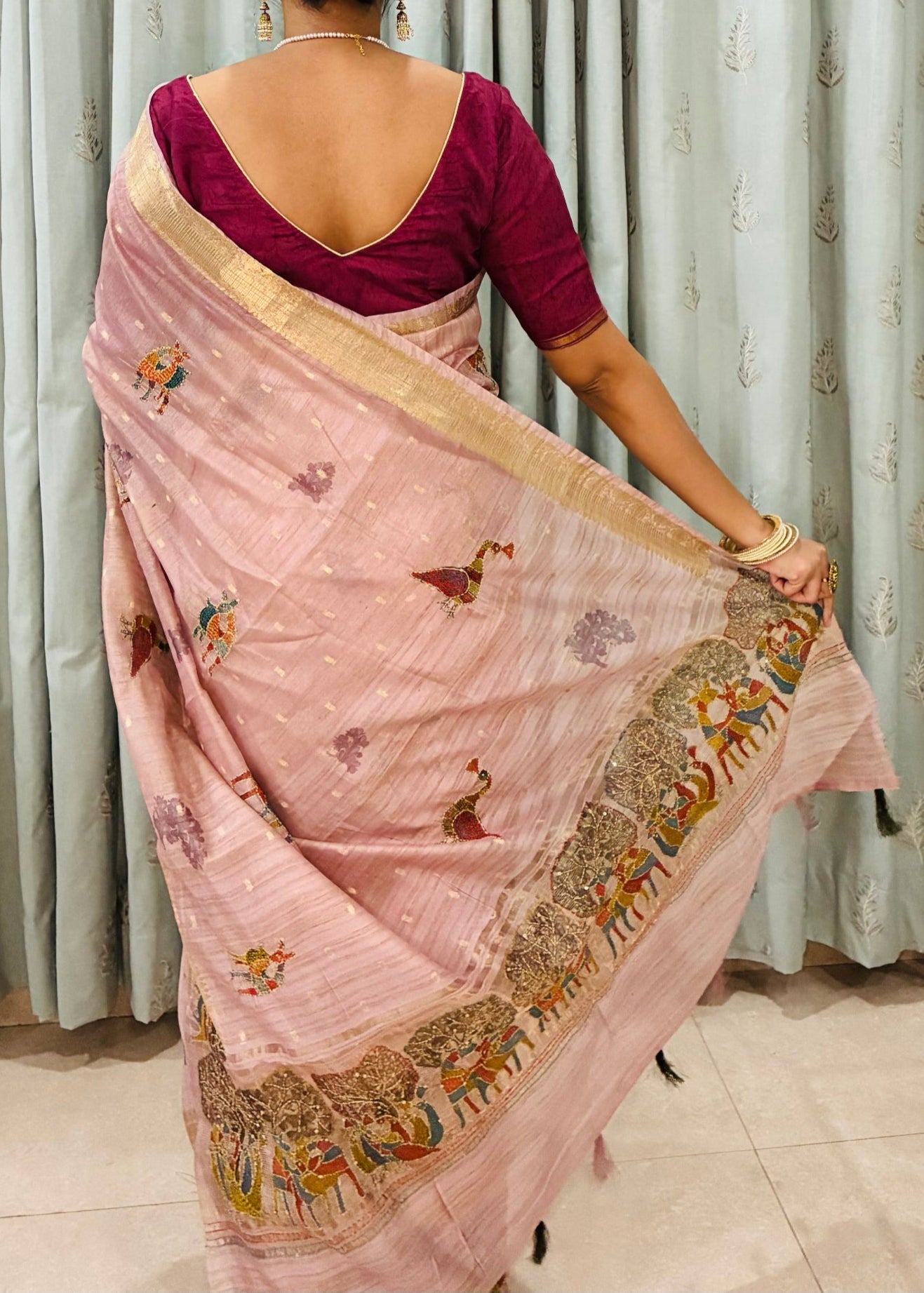 Woman wearing a pink saree with a maroon blouse in front of a curtain.