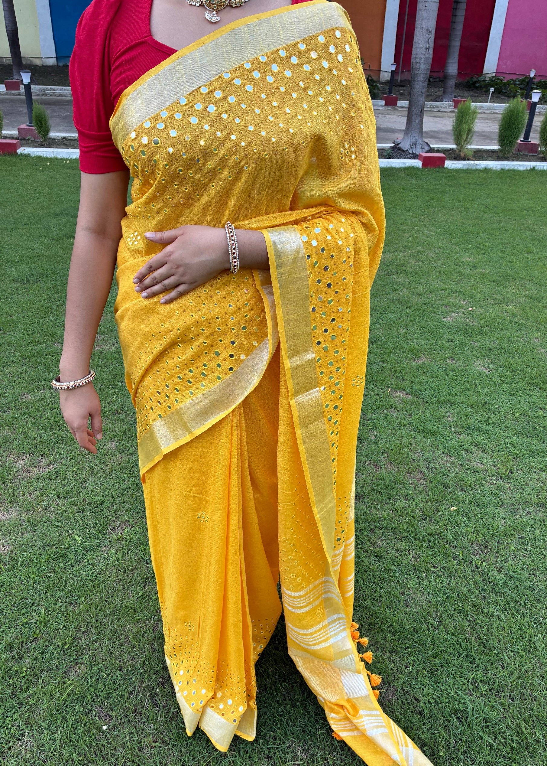 Person wearing a yellow saree with a red blouse on a grassy background