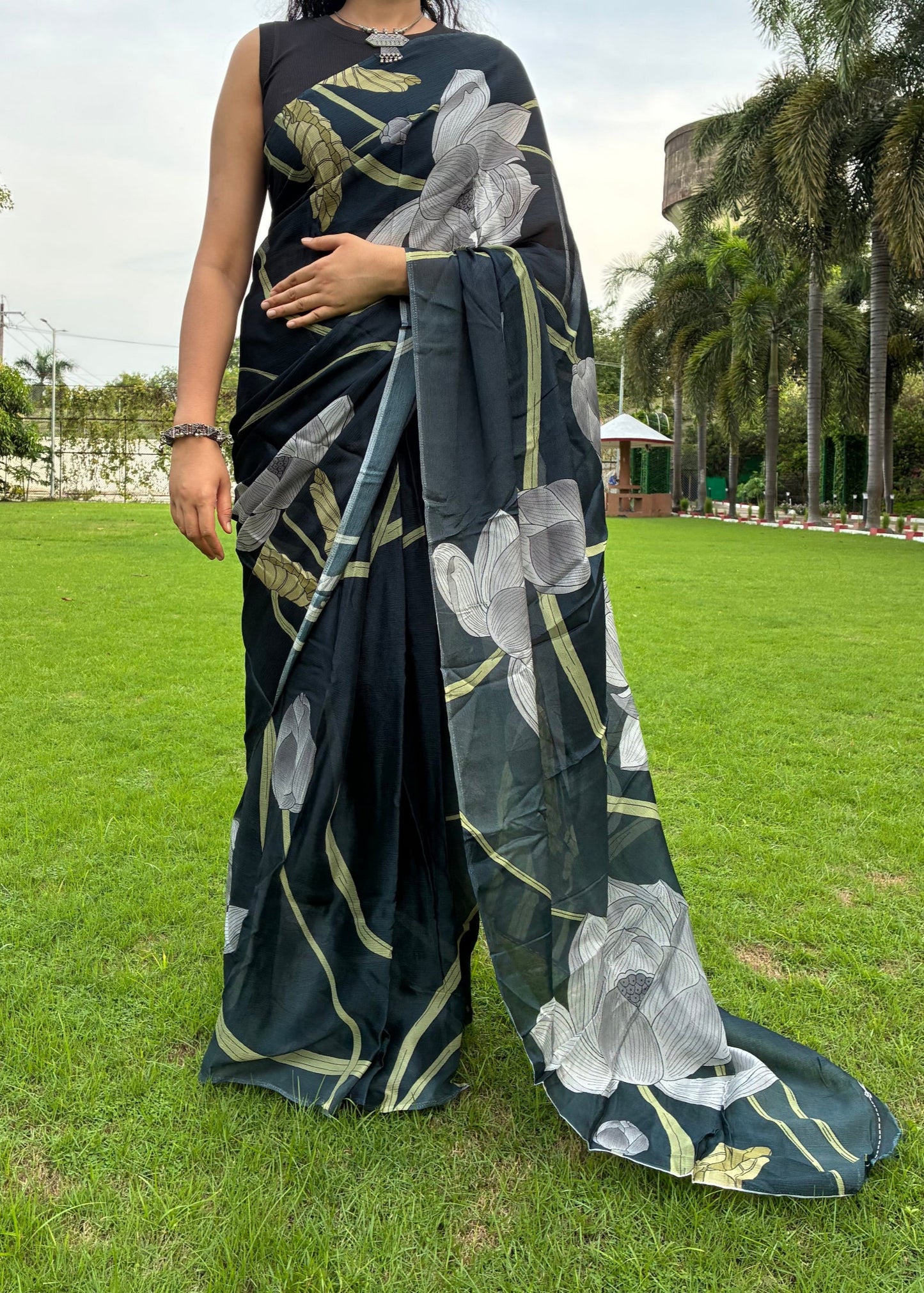 Woman wearing a black saree with floral patterns standing on grass