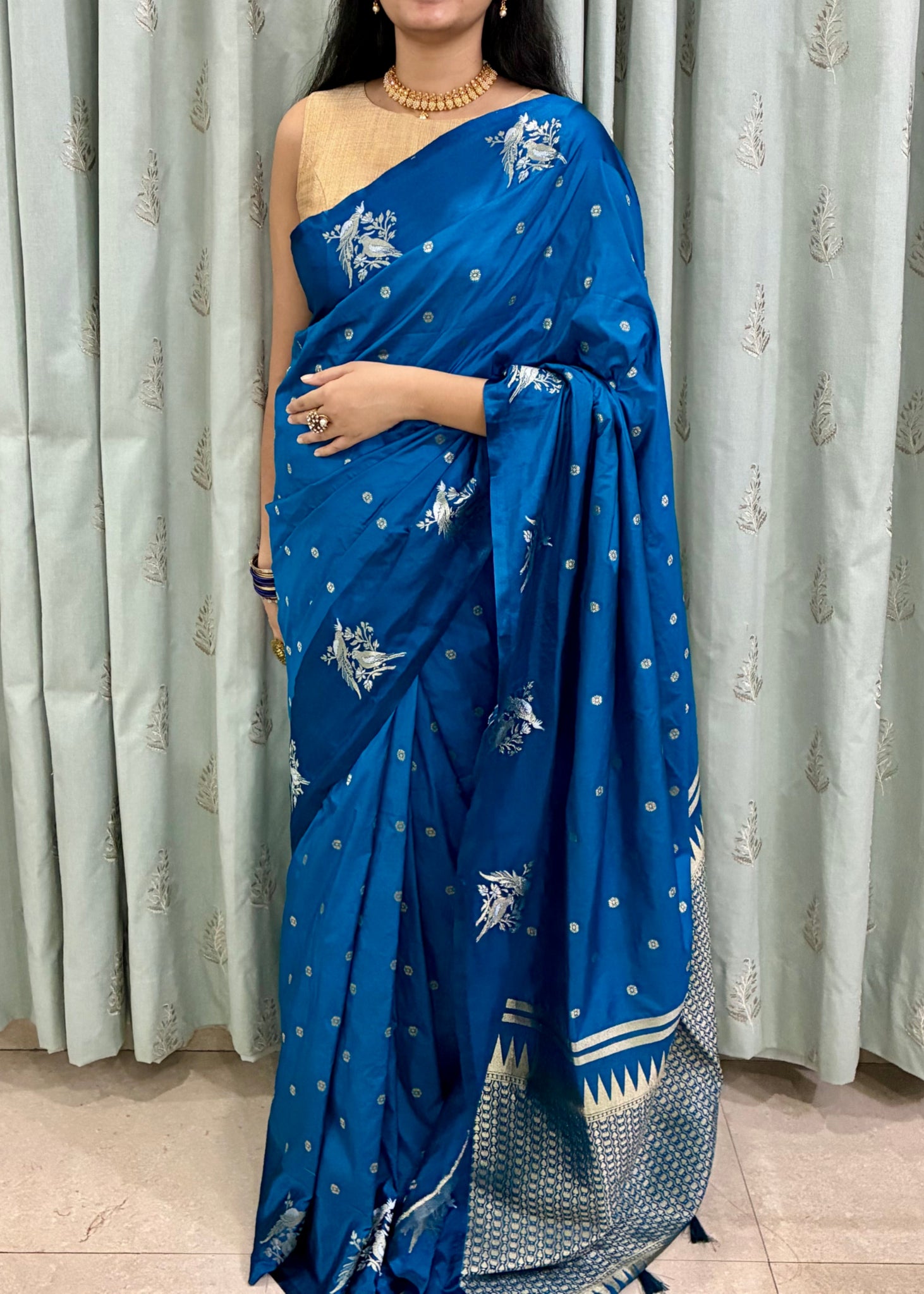 Woman wearing a blue saree with white patterns against a light curtain background