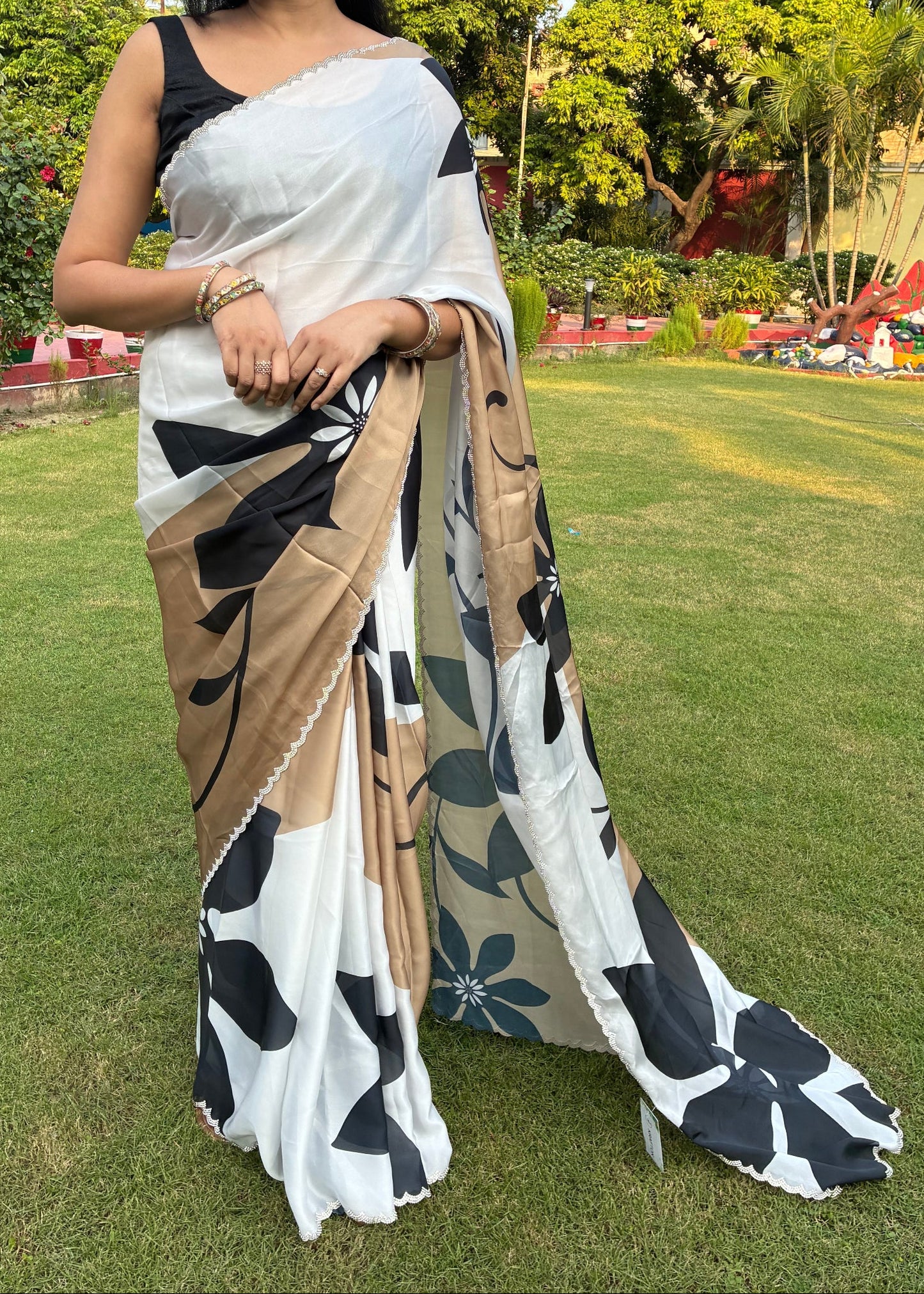 Woman in a saree standing outdoors with greenery in the background