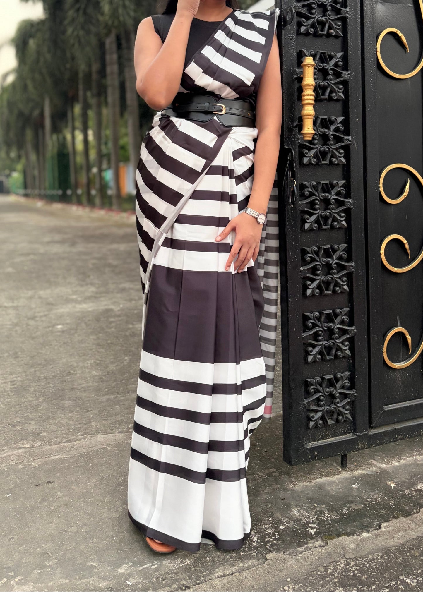 Woman in a black and white striped dress standing in front of an ornate gate.