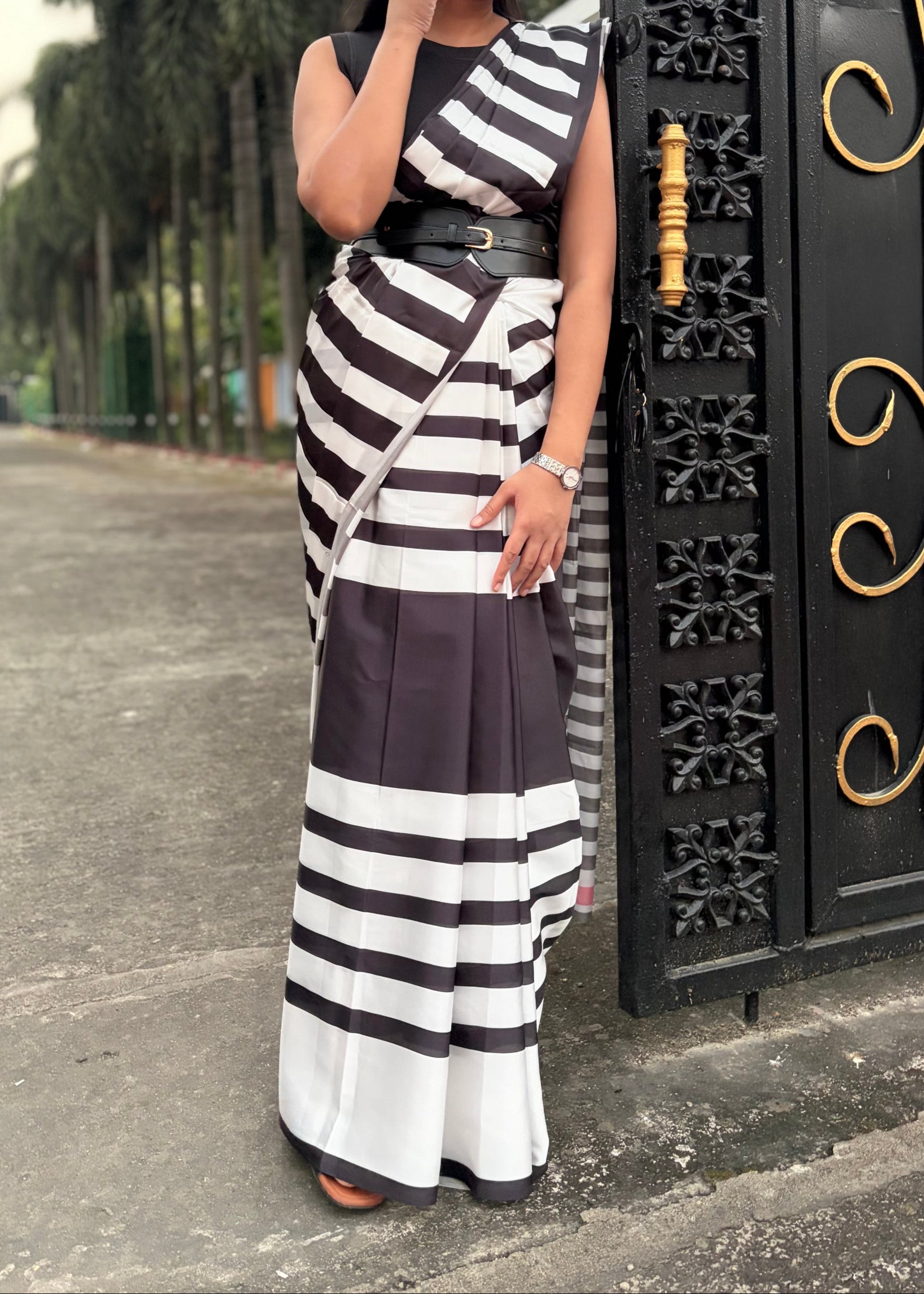 Woman in a black and white striped dress standing in front of an ornate gate.