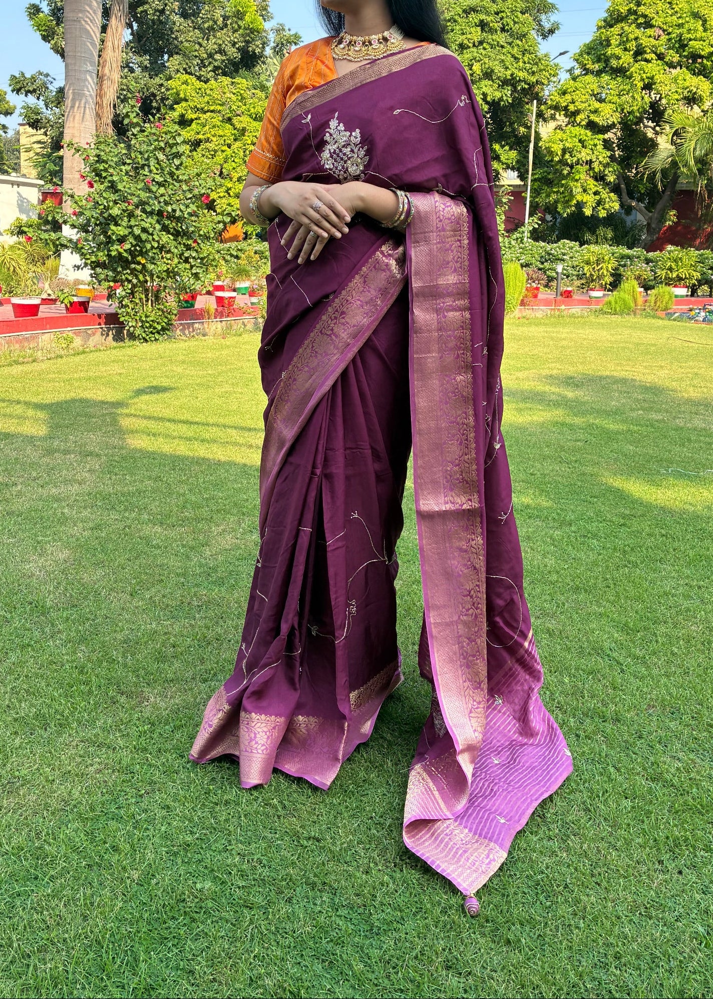 Person wearing a purple saree with a green field and trees in the background