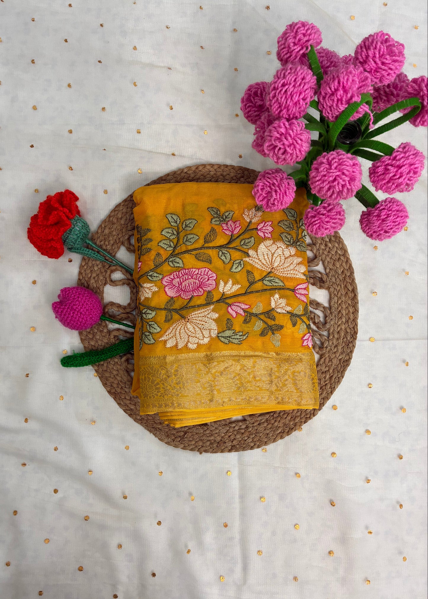 Yellow embroidered fabric with floral patterns on a textured surface with pink and red flowers.