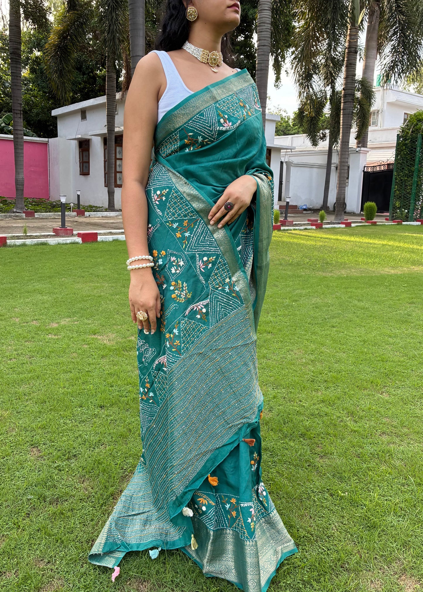 Woman in a green saree standing on grass with palm trees in the background
