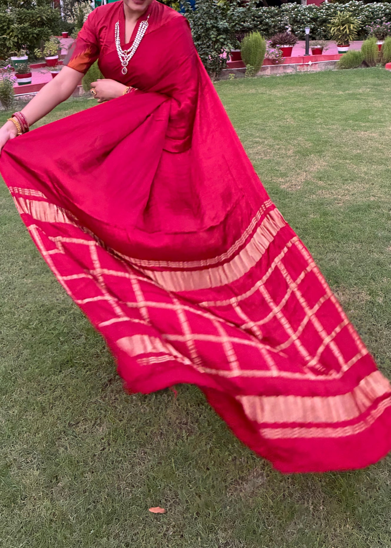 Person wearing a red saree with a pattern on a grassy area
