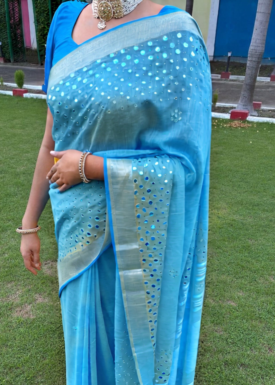 Woman wearing a blue saree with white patterns on a grassy background