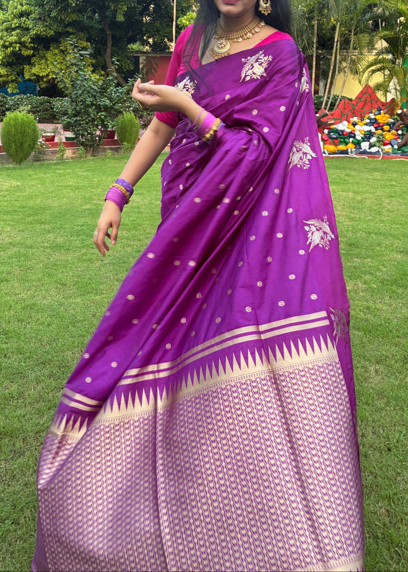 Woman in a purple saree standing on grass with trees in the background