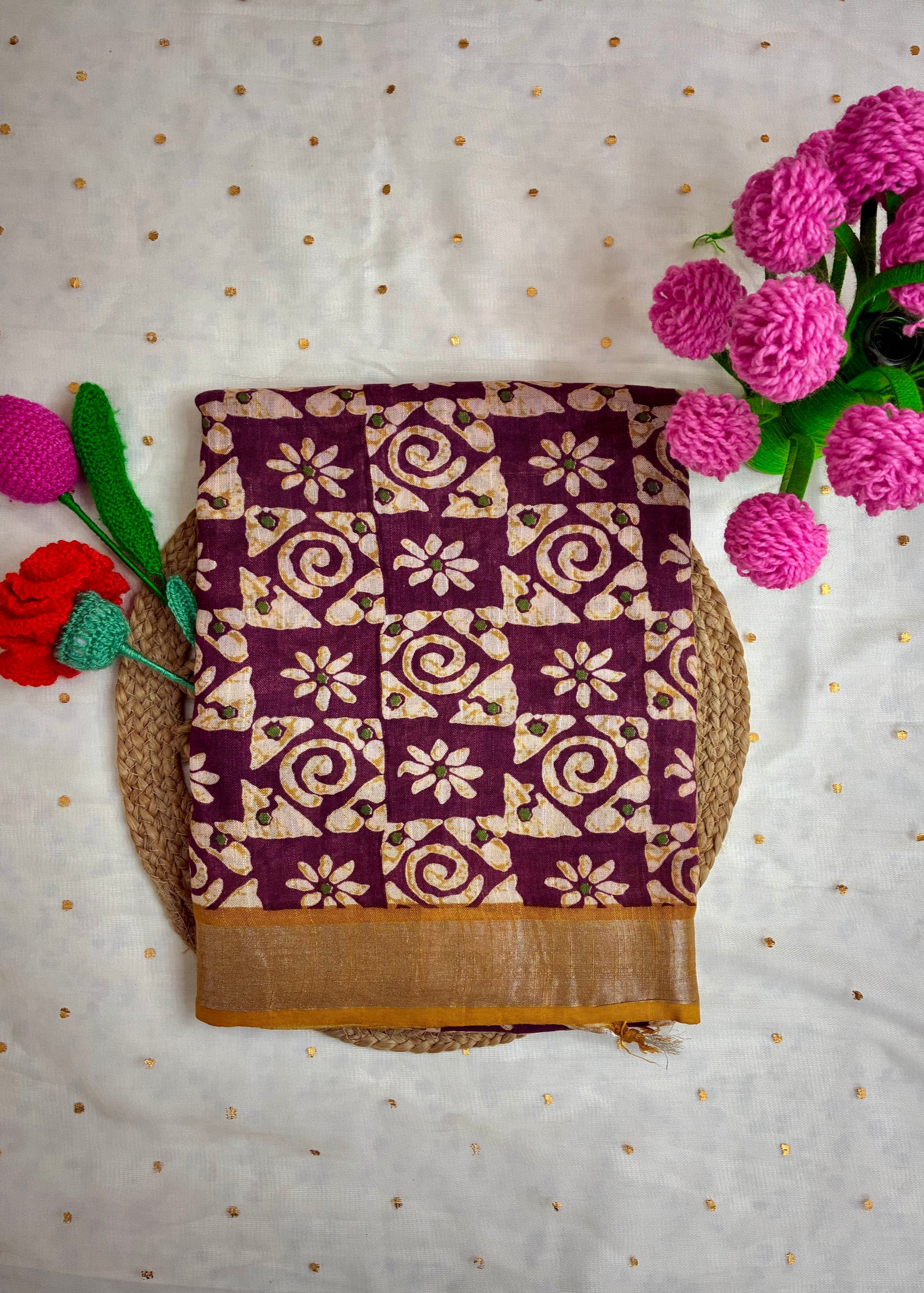 Folded fabric with purple and beige pattern on a light background with flowers.