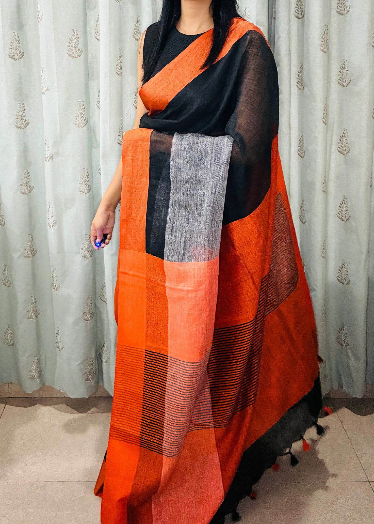 Person wearing an orange and black checkered scarf in front of a patterned curtain.