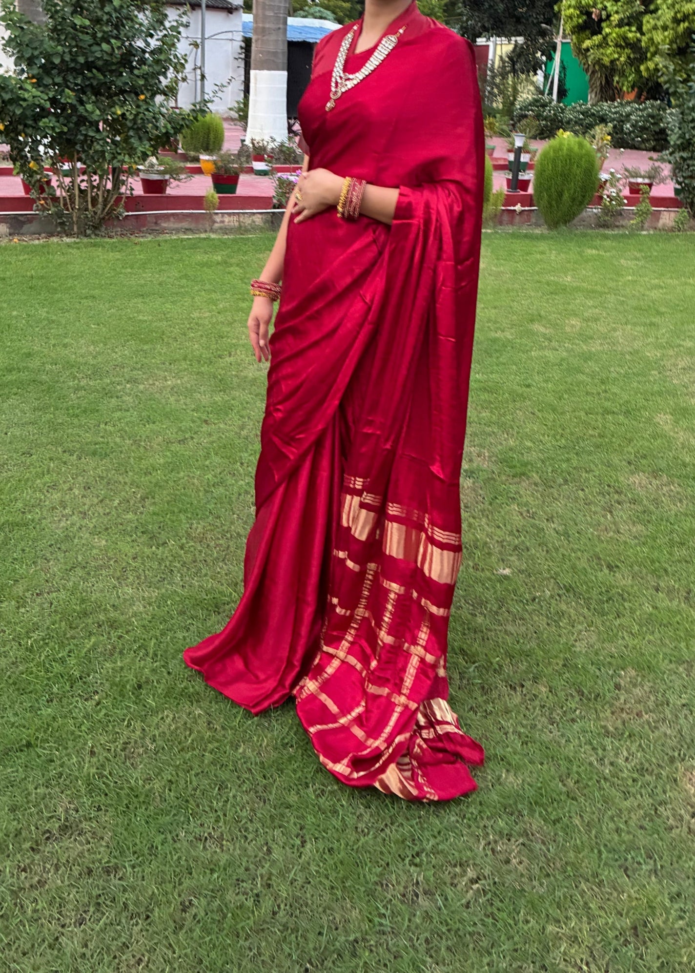 Woman in a red saree standing on grass with trees in the background