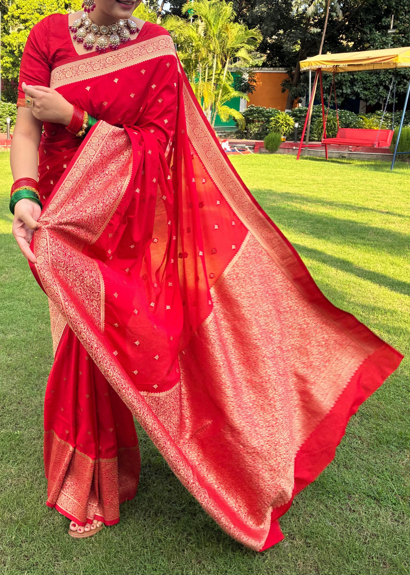 Person wearing a red saree with a green outdoor background