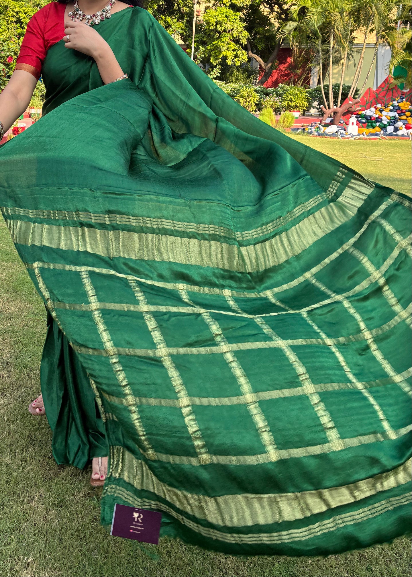Woman in a green saree with a checkered pattern standing outdoors with trees in the background