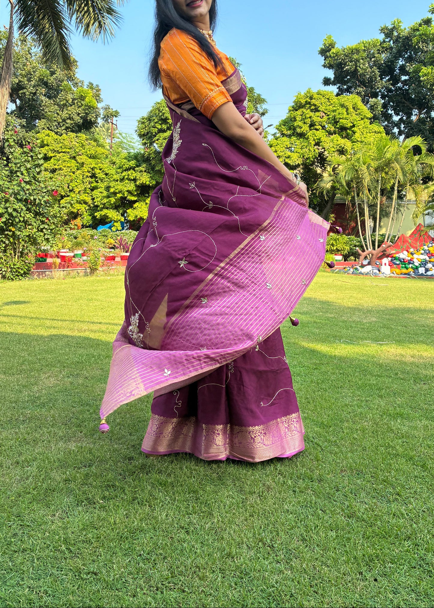 Woman in a purple saree standing on grass with trees in the background