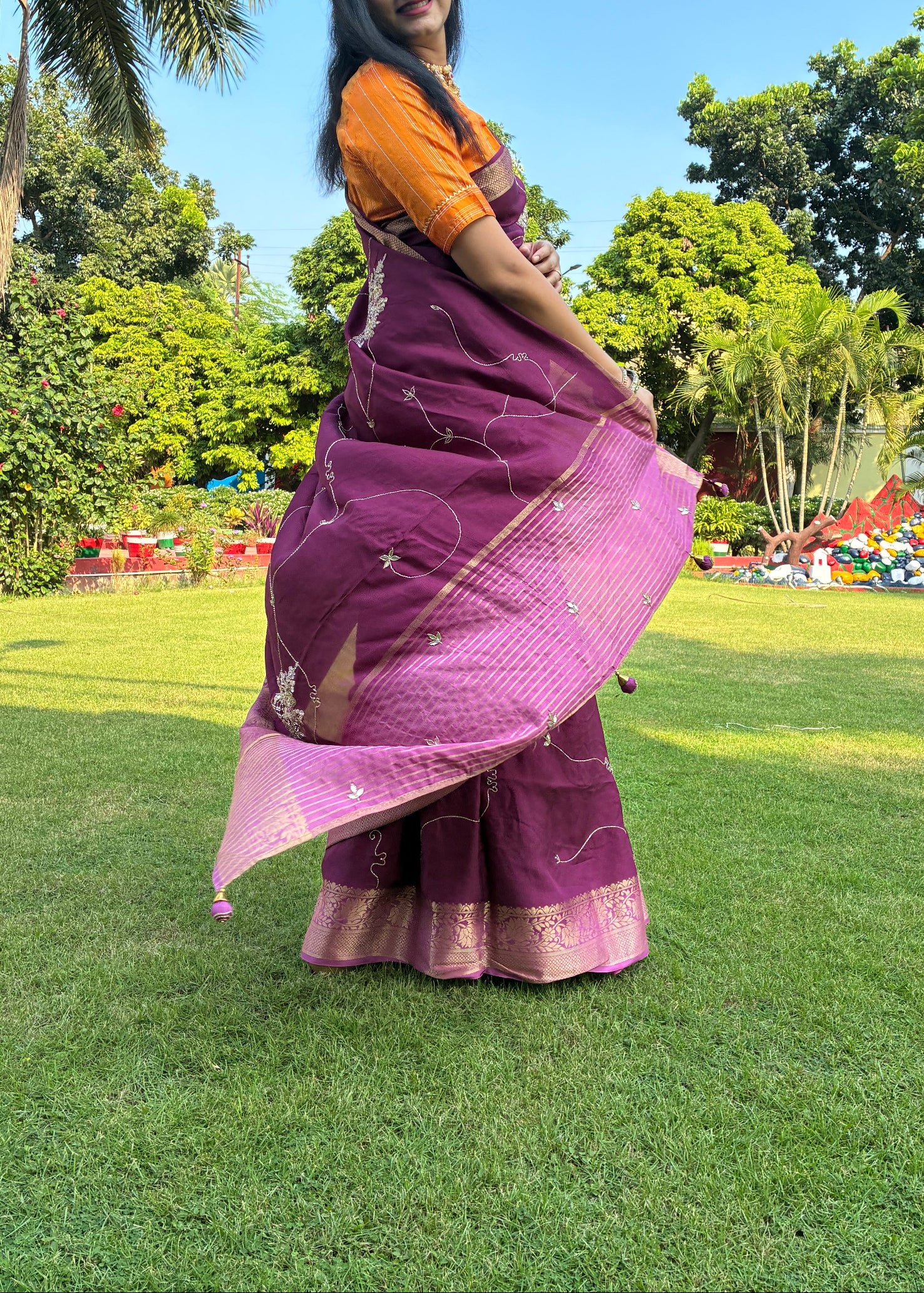 Woman in a purple saree standing on grass with trees in the background