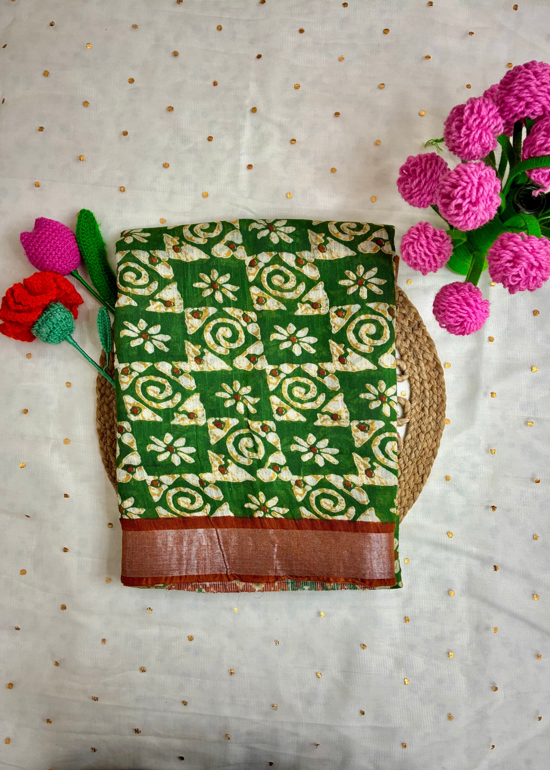 Green and white patterned fabric with brown border on a light background with flowers.