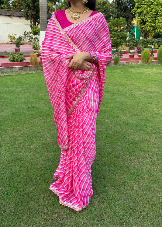Woman in a pink saree standing on a grassy area with trees in the background
