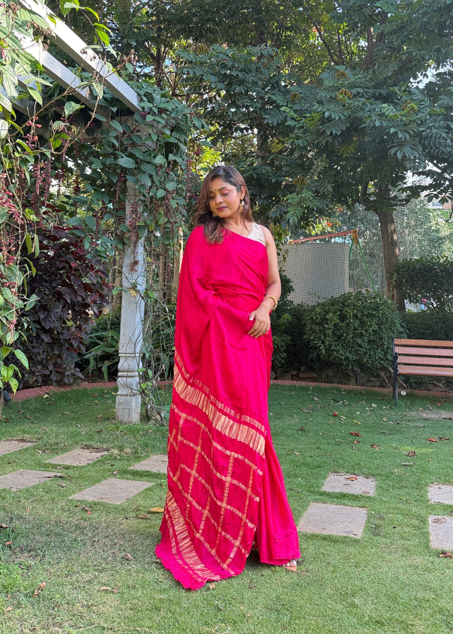 Person in a red saree standing outdoors with greenery around