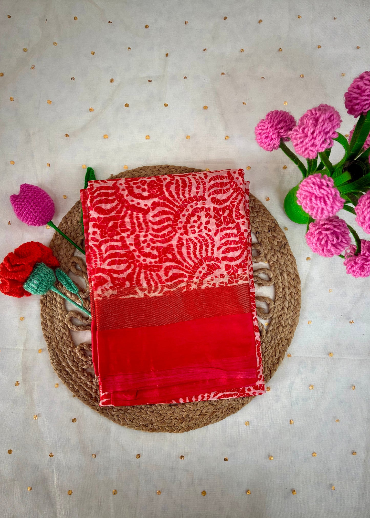 Red and white patterned fabric on a woven mat with pink flowers on a light background