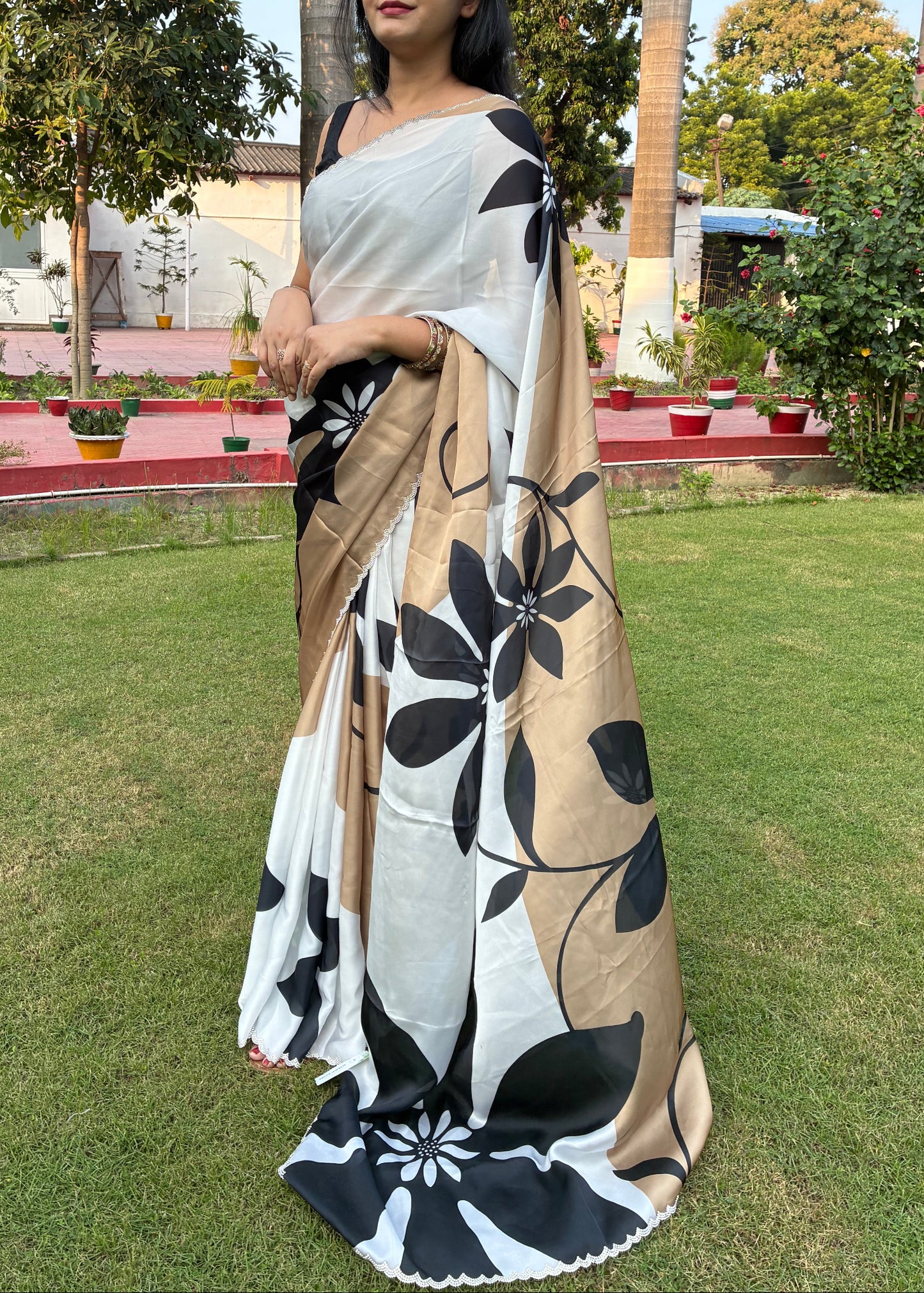 Woman holding a black and white floral-patterned scarf in an outdoor setting with trees and grass.