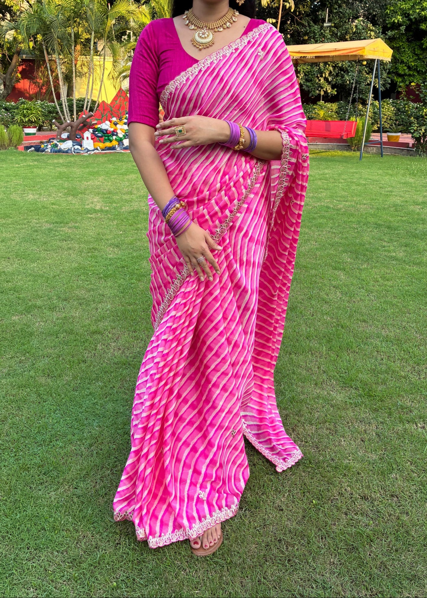Woman in a pink saree standing on grass with trees in the background