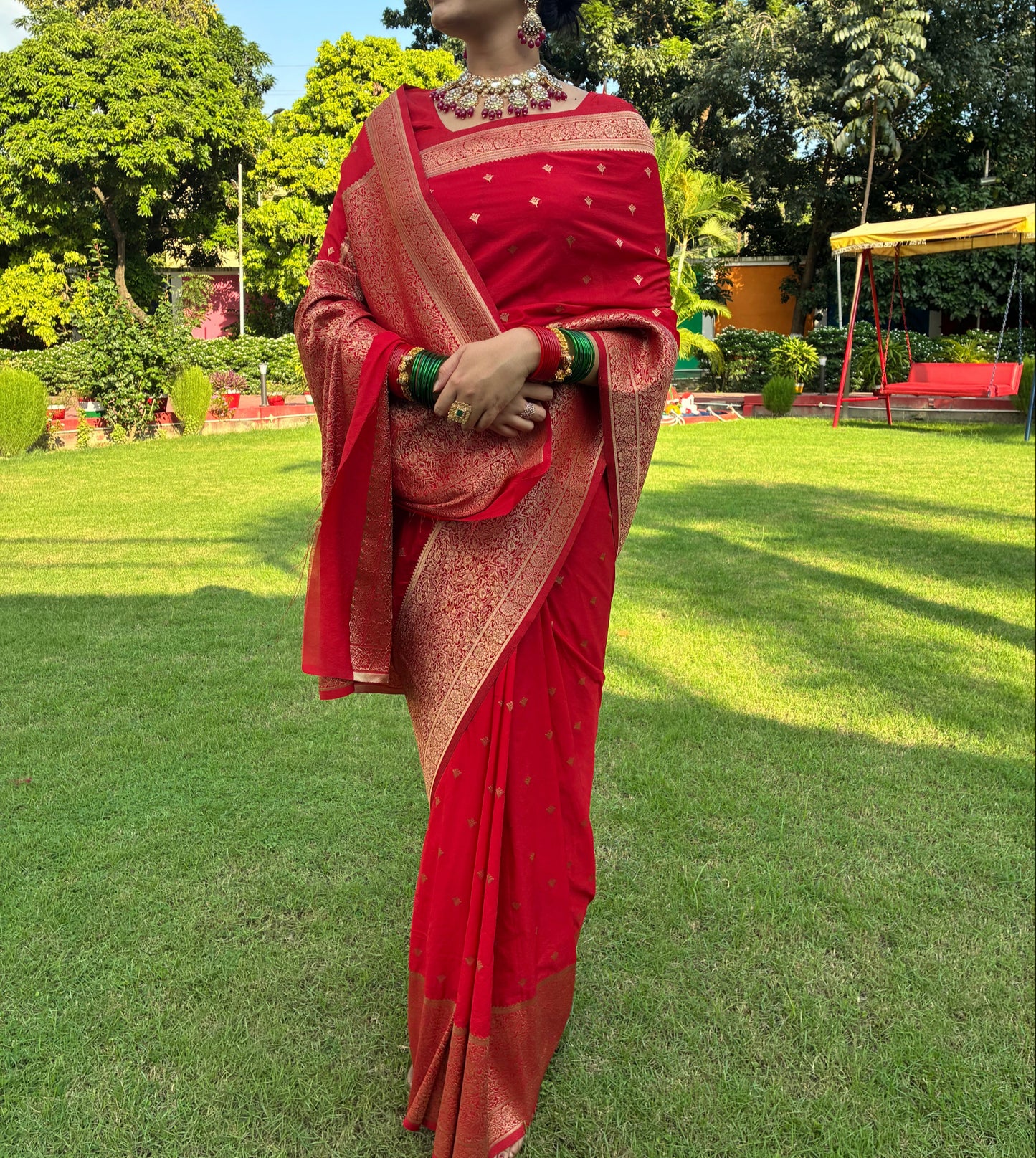 Woman in a red saree standing on grass with trees in the background