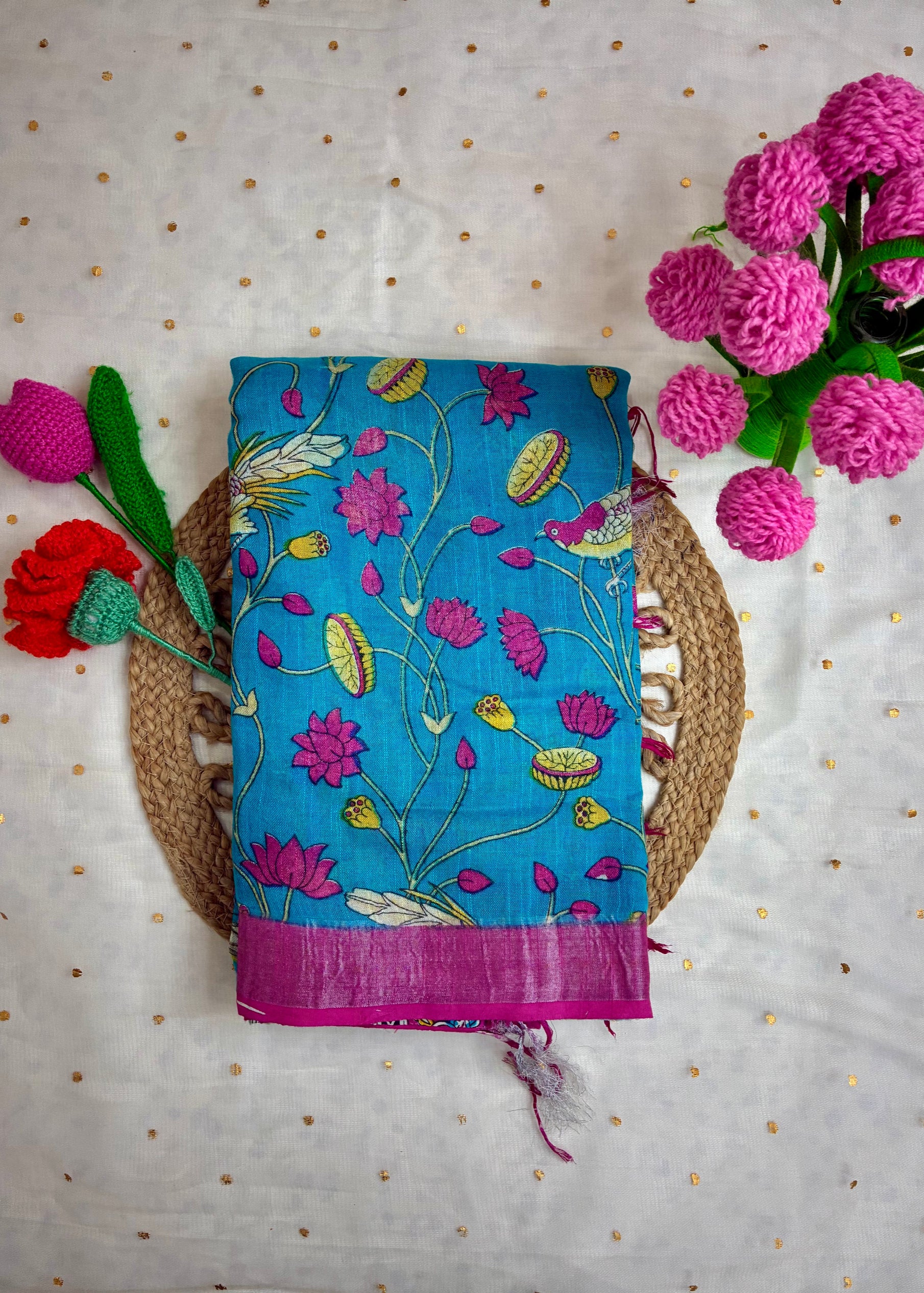 Blue embroidered fabric with pink flowers on a textured surface with flowers around