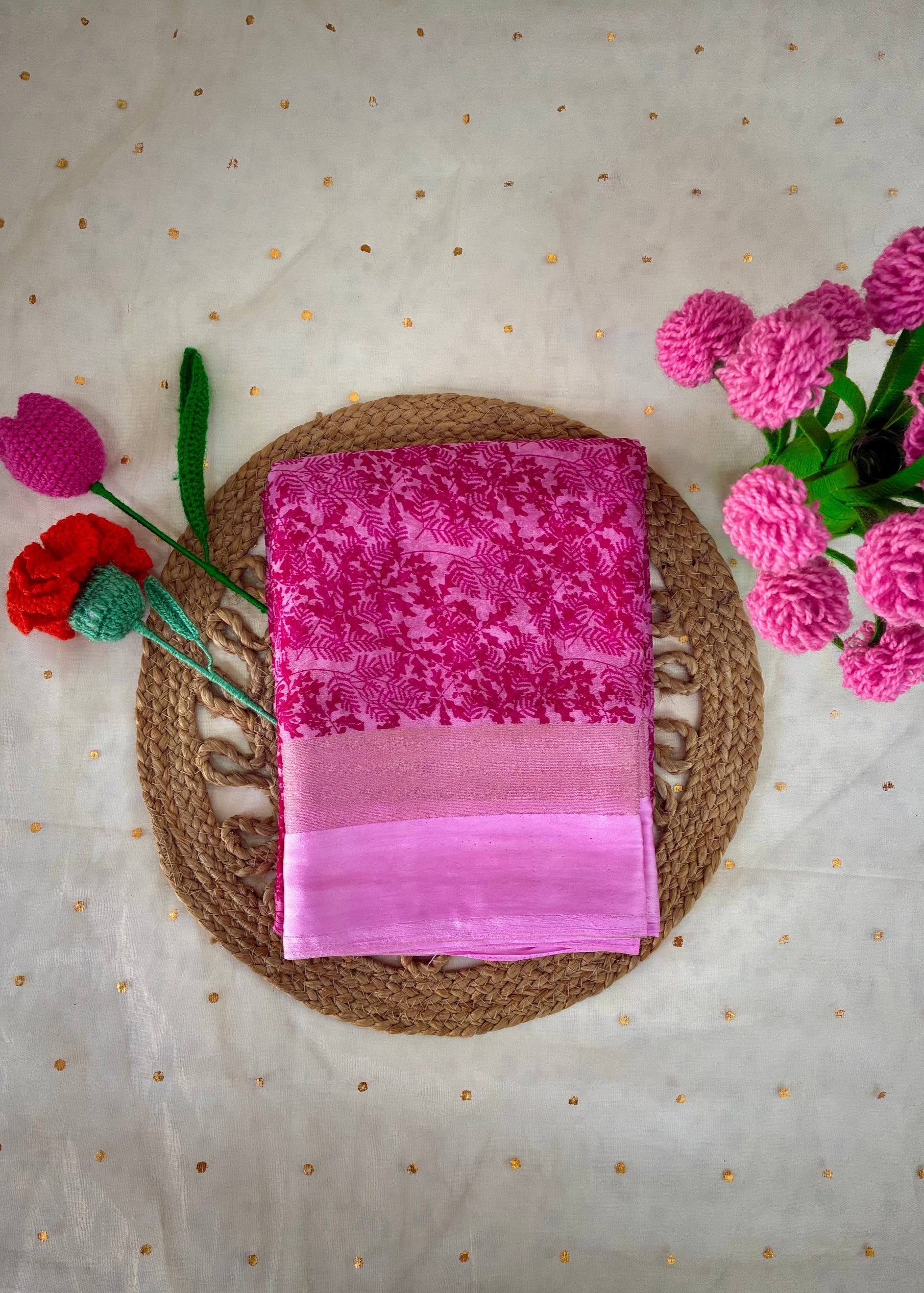 Pink saree with floral patterns on a textured surface with flowers around