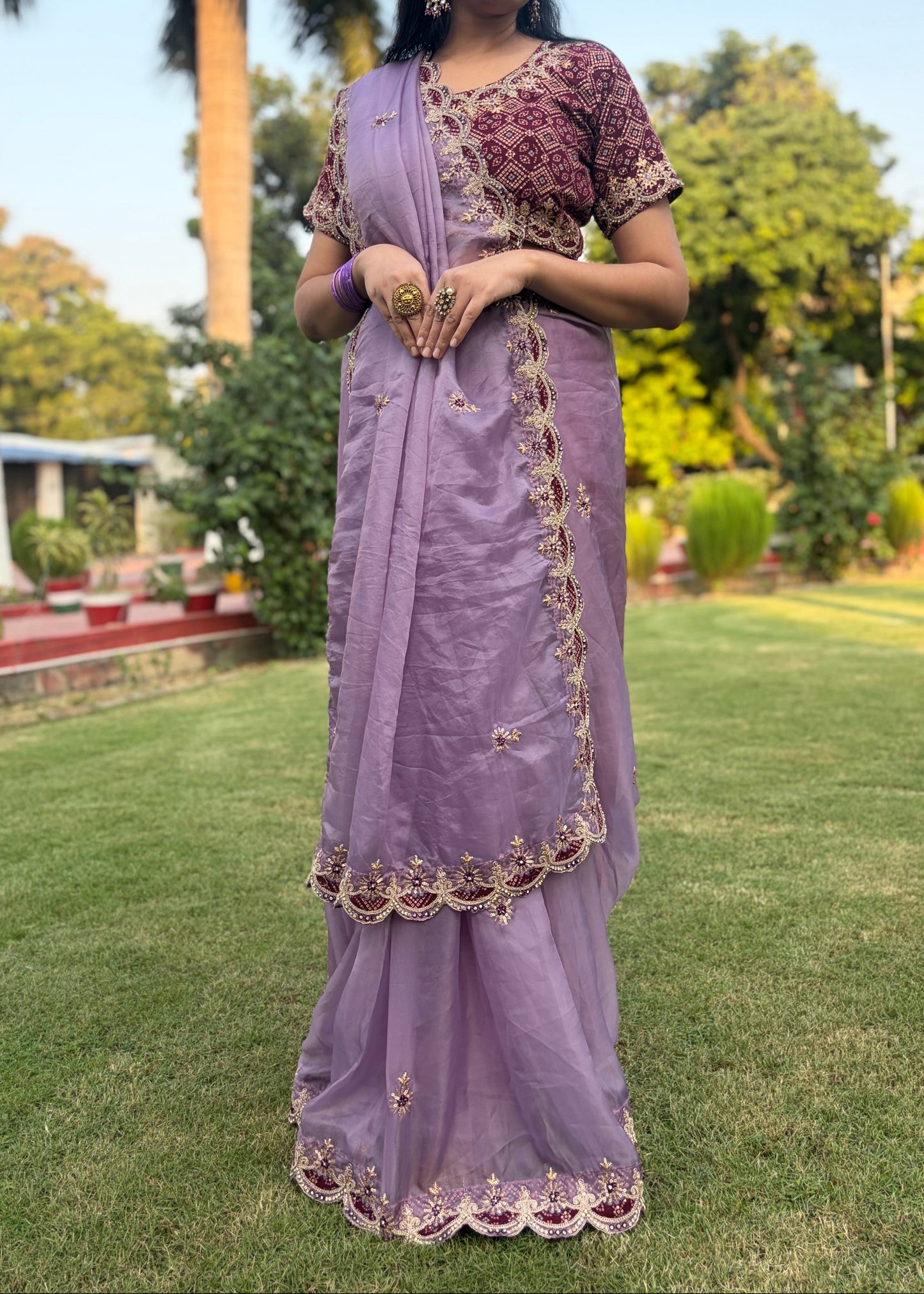 Woman in a lavender saree with a floral blouse standing outdoors on grass