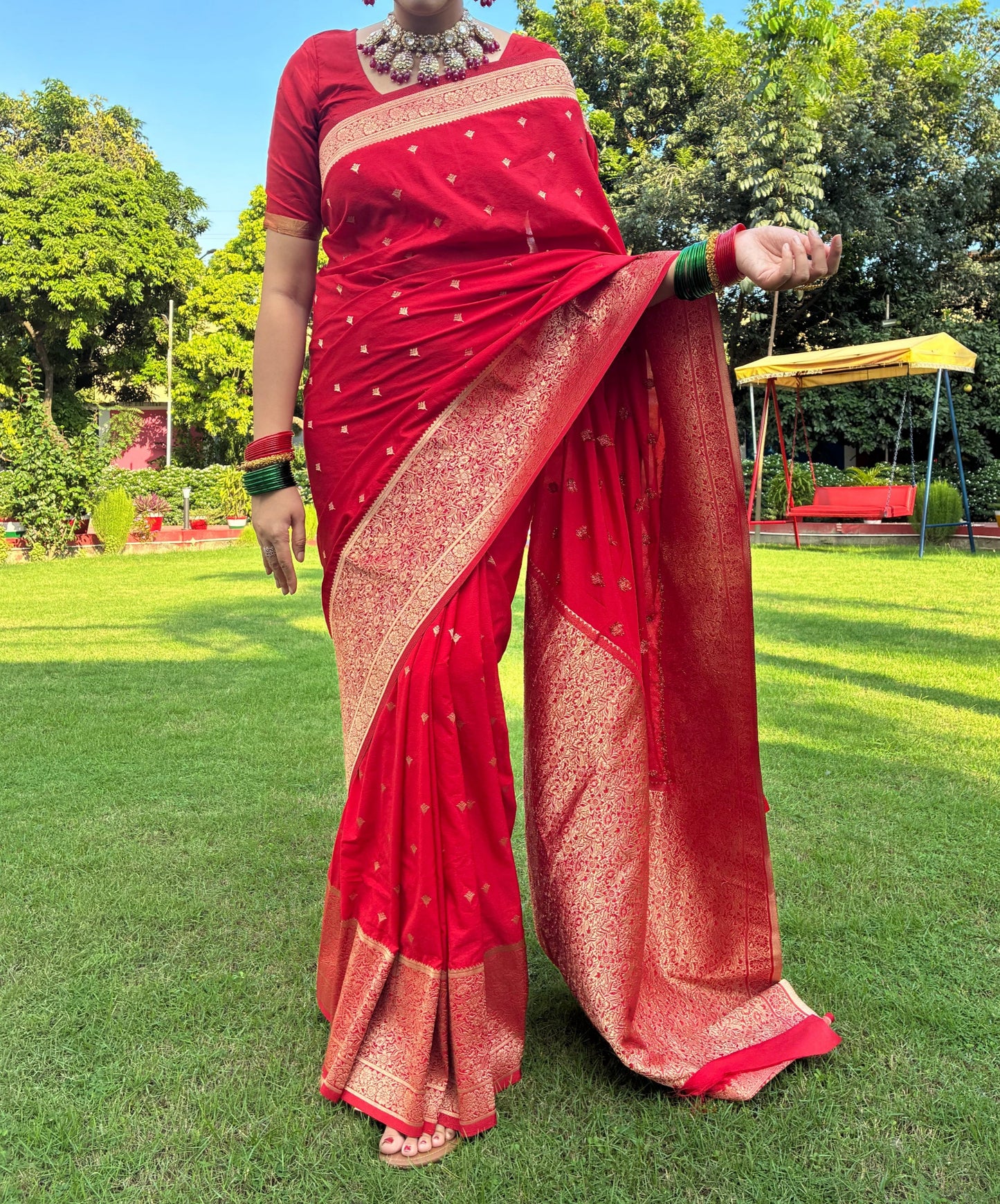 Person wearing a red saree standing on grass with trees in the background
