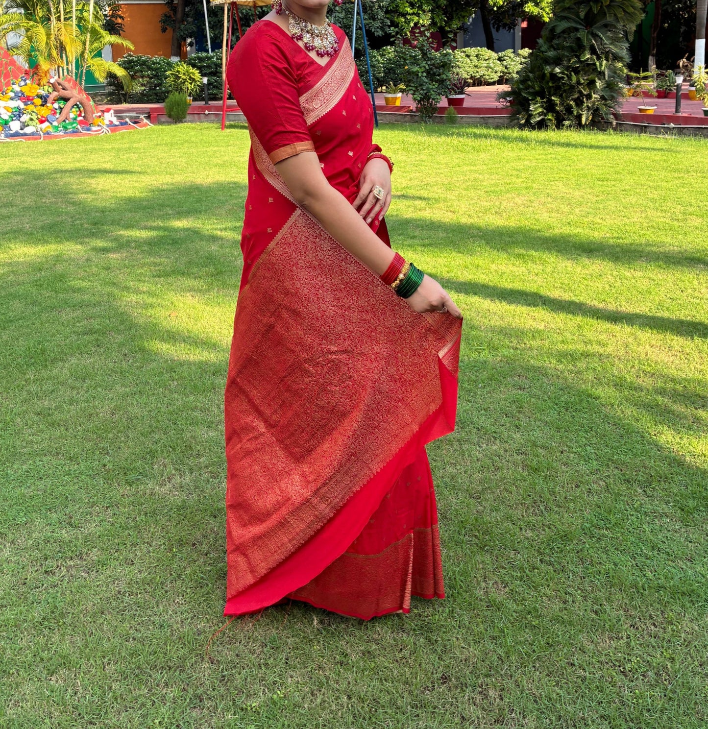 Person in a red saree standing on grass with trees in the background