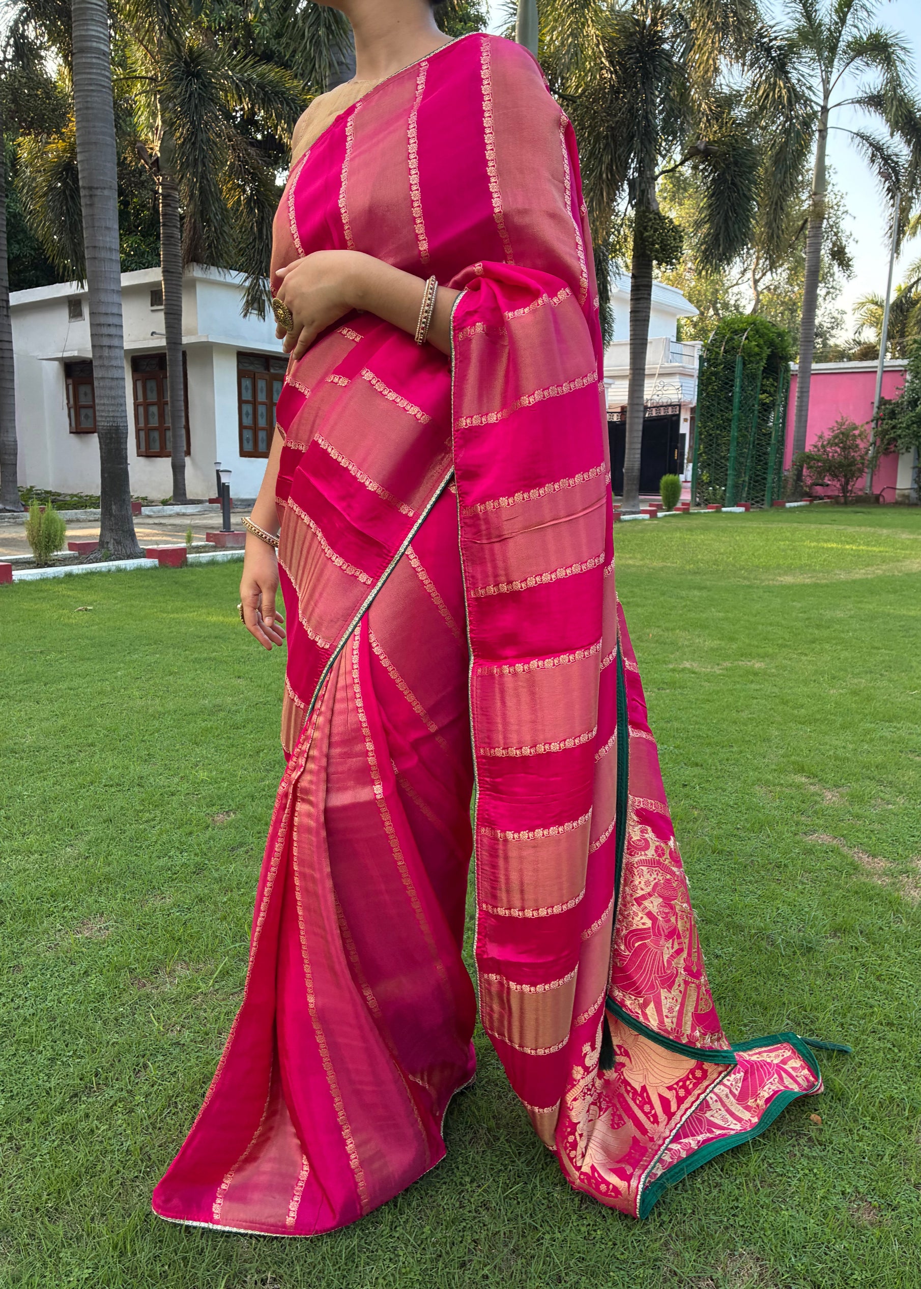 Person wearing a pink saree with a blurred background of green grass and trees