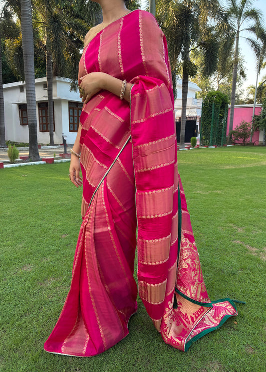 Person wearing a pink saree with a blurred background of green grass and trees