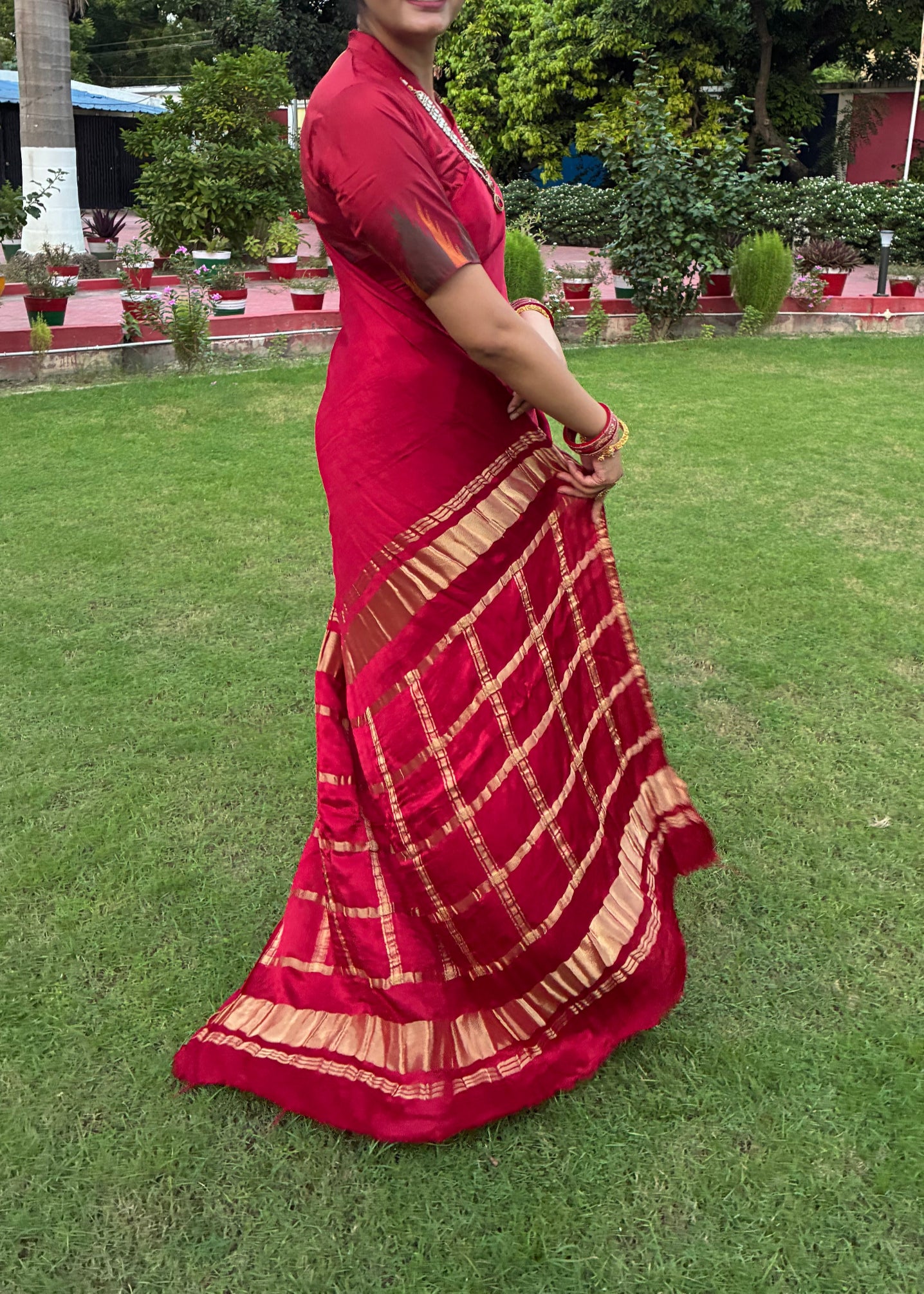 Person wearing a red saree standing on grass with trees in the background