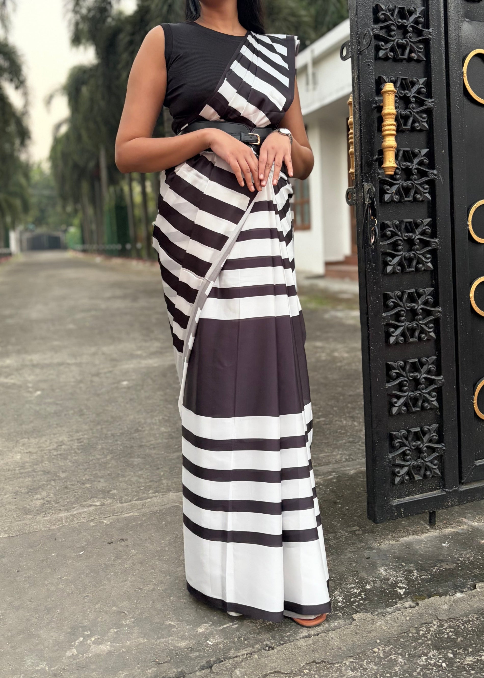 Woman wearing a black and white striped dress standing next to a decorative metal gate.