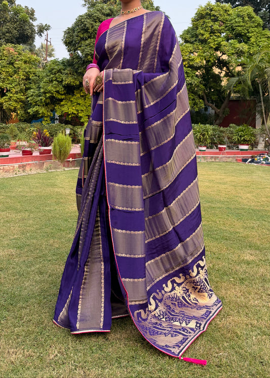 Woman wearing a purple and gray striped saree in an outdoor setting with greenery.