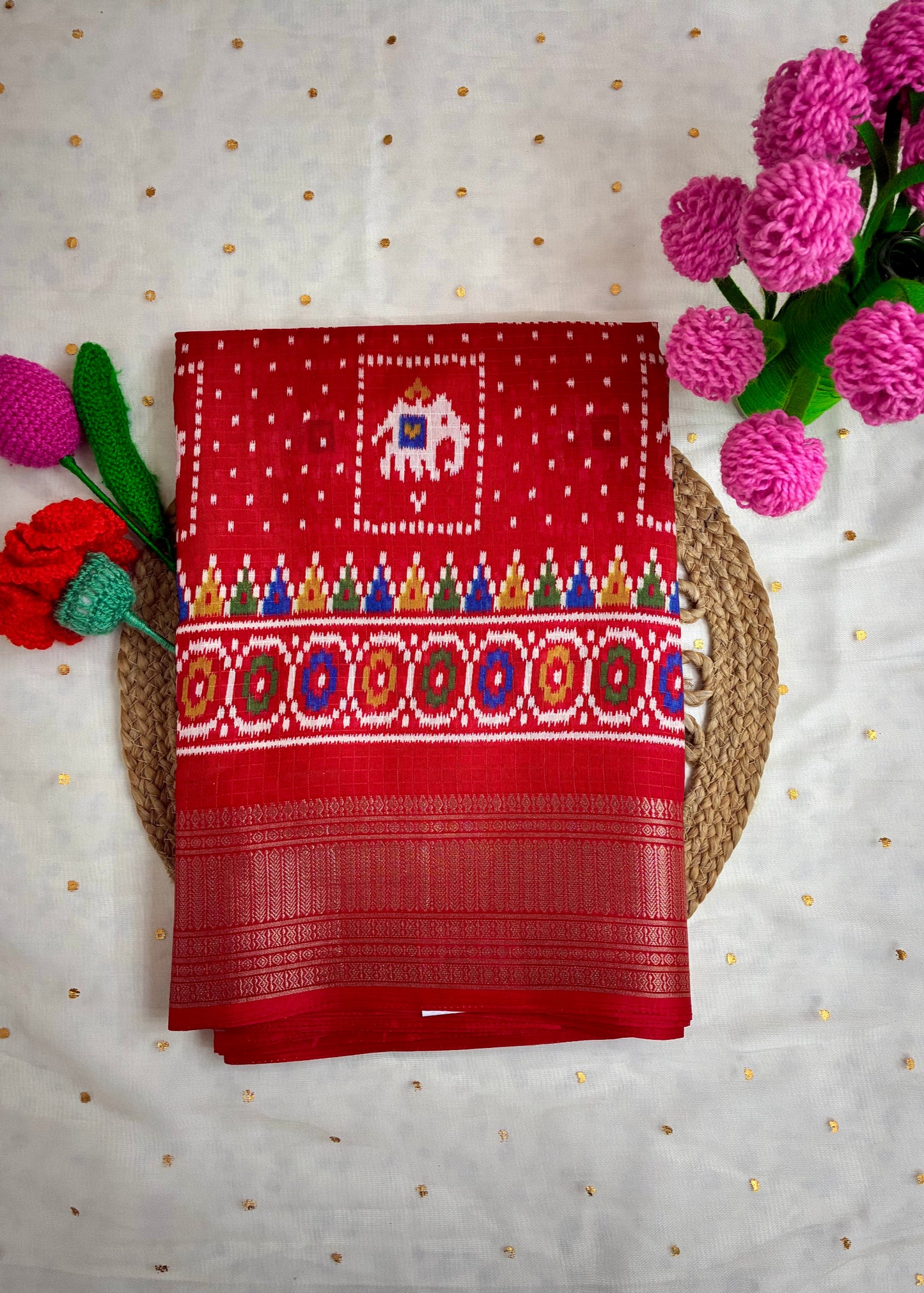 Red fabric with intricate patterns on a white background with pink flowers.
