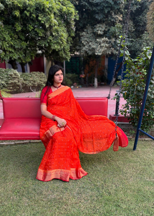Woman in an orange saree sitting on a pink bench in a garden.