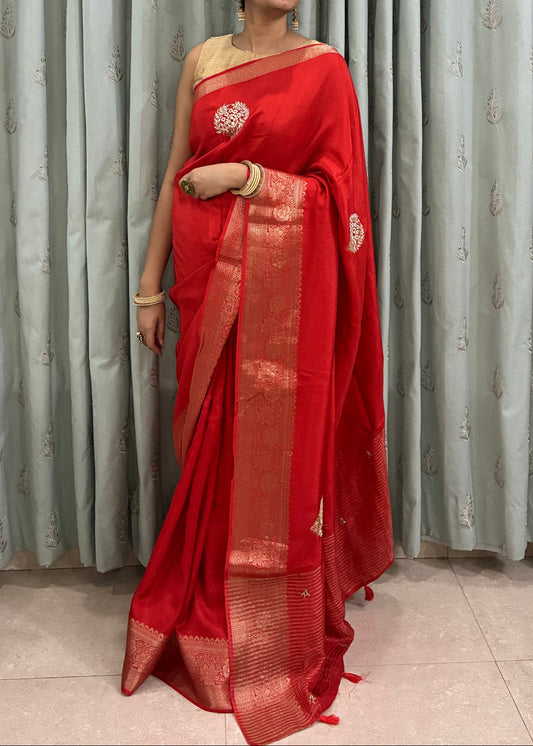 Person wearing a red saree standing in front of corrugated metal sheets.