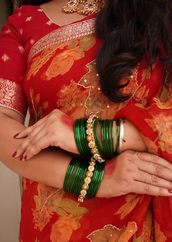 Person wearing a red saree with floral patterns and green bangles.